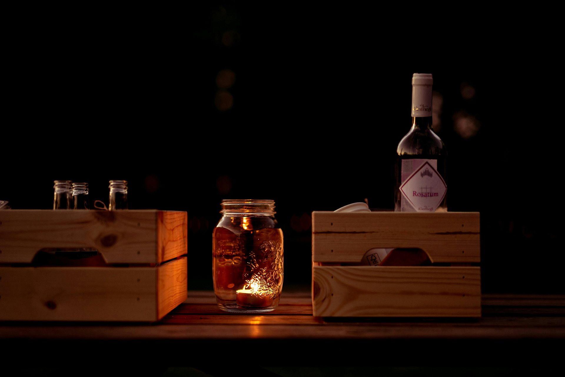Photo of a table holding two wood boxes containing wine bottols and a mason jar candle between them take by Laura Adai