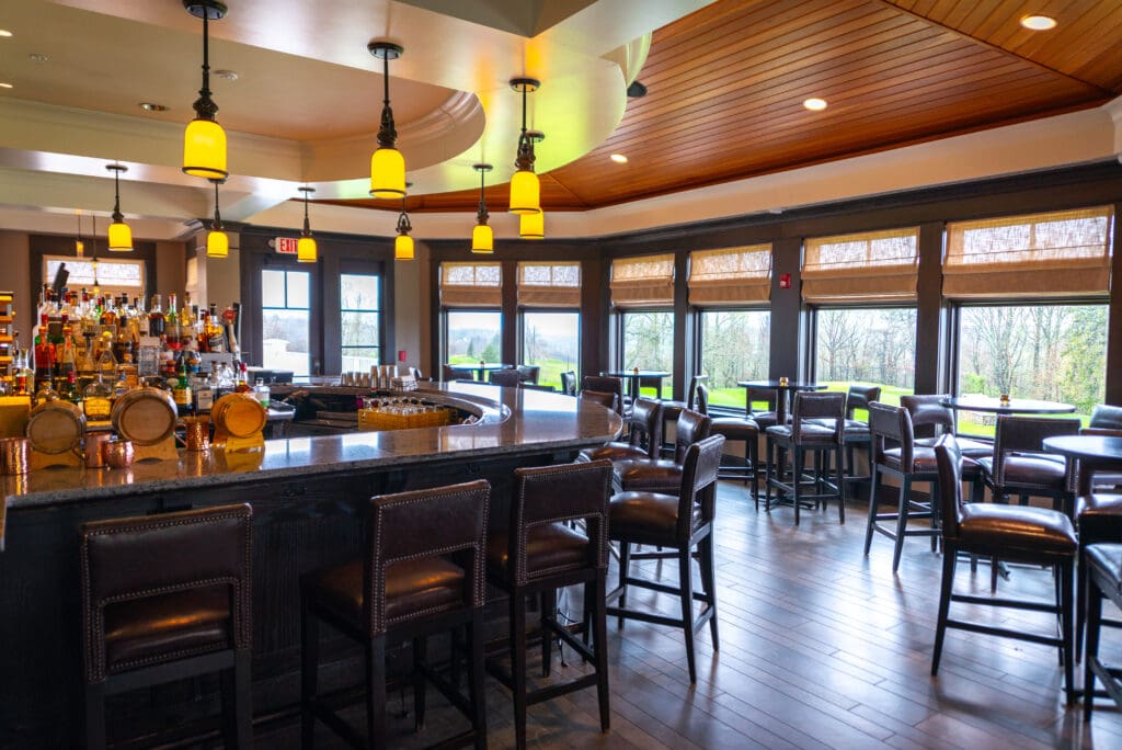 Curved granite bar with leather stools and amber pendant lights in a golf club clubhouse, with windows overlooking the course