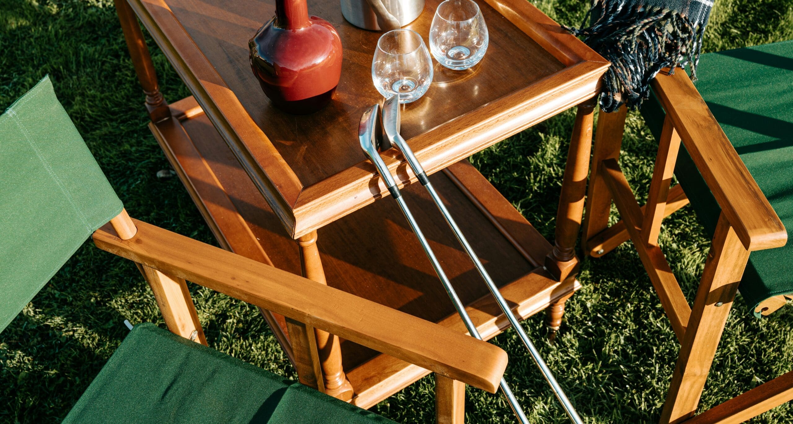 golf-country-club-bar-cart-irons Two golf irons leaning against a bar cart with wine glasses on the lawn at a golf and country club